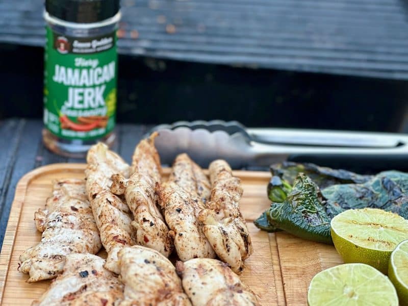 cutting board of Jamaican Jerk Chicken Tenders at the grill with the spice shaker and limes