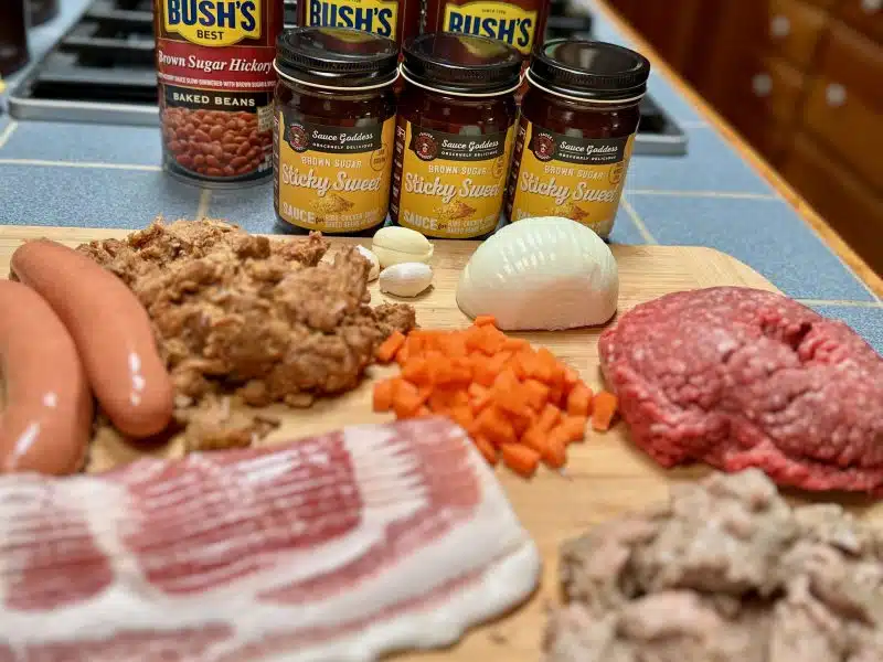 The ingredients for cowboy beans:bacon, italian sausage, hot dogs, ground beef, carrots, onion, garlic, pulled pork, Sauce Goddess sticky Sweet sauce and baked beans.