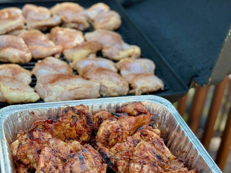 A grill full of Chicken cooking and a pan full of grilled chicken with Sweet & Spicy sauce